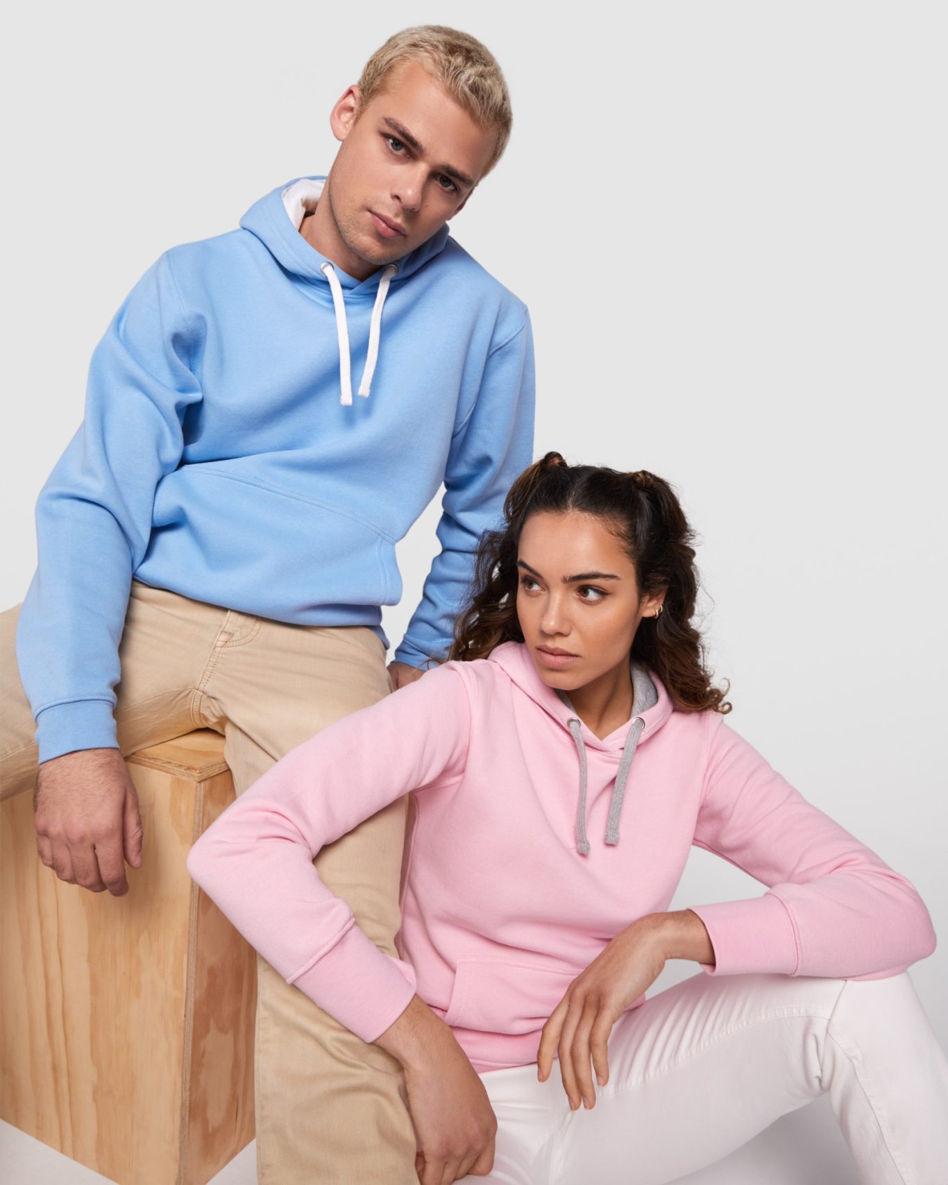 Sudadera URBAN Jóvenes modelos luciendo sudaderas azules y rosas, sentados sobre un banco de madera.