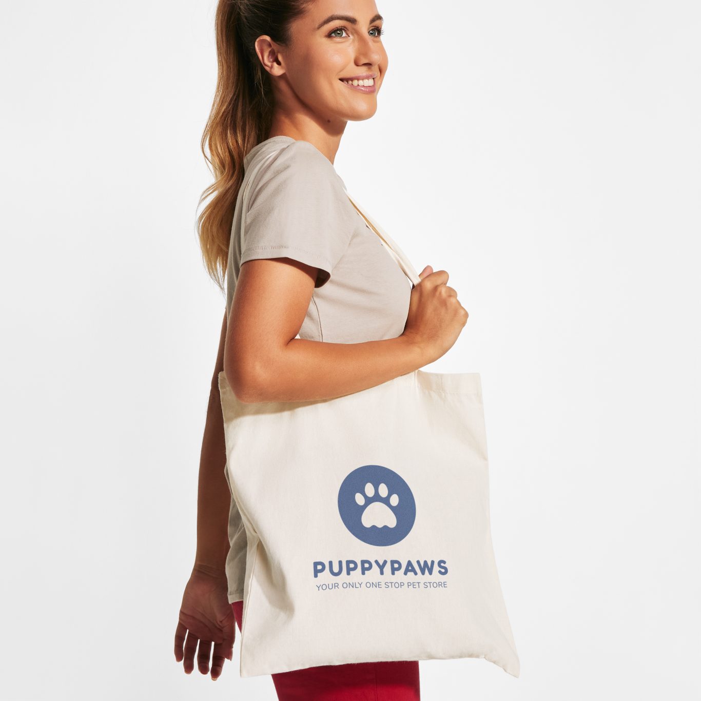 Tote bag HILL Mujer sonriente sostiene una bolsa de tela con el logo "PuppyPaws".